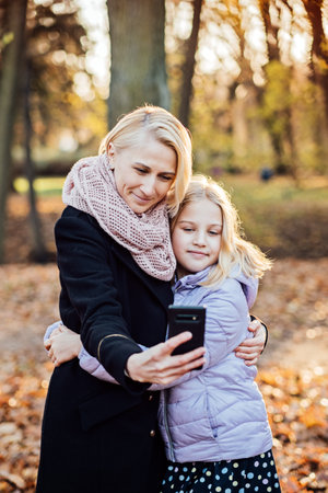 Parent-child bonds and mother daughter relationships. Mother and daughter embracing, capturing a special moment selfie together amidst the golden hues of autumn.の写真素材