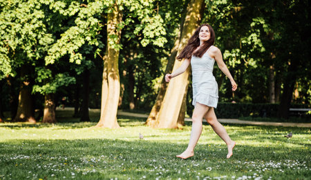 Joyful Woman Walking Barefoot in City Parkの写真素材