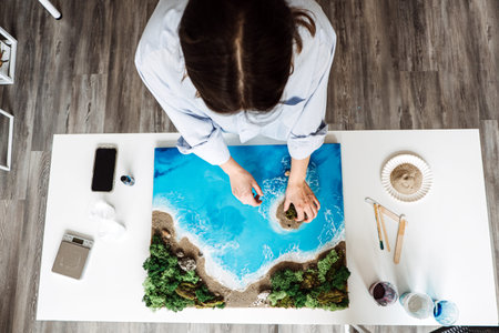 Creating beautiful epoxy resin art at home, featuring a coastal scene with vibrant blue waters,...