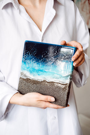 Close-up of person holding ocean-inspired resin art piece, showcasing detailed craftsmanship and unique design. Handmade coastal-themed home decor.の写真素材