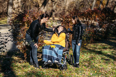 Mother and sibling providing emotional support to child in wheelchair, disability care, family strength, special needs support, outdoor bonding.の写真素材