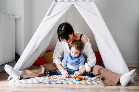 Mother playing with toddler in makeshift indoor tent. Early childhood development, role of play, motor skills, cognitive growth, parent-child interactionの写真素材