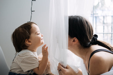 Mother and child sharing a playful moment by the window. Bonding, early childhood, indoor play, mother-child interaction, family timeの写真素材