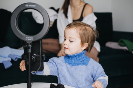 Curious toddler interacting with ring light during family video shoot. Behind the scenes, content creation, family fashion, child exploration, digital mediaの写真素材