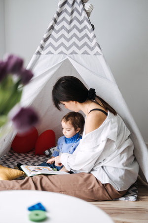 Mother reading to toddler inside indoor tent. Play space design, indoor tents, home activities, engaging environments, child-friendly spacesの写真素材