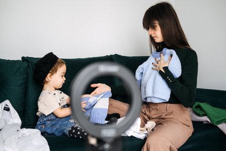 Mother and toddler selecting matching outfits on a couch. Family fashion, coordinated outfits, matching styles, fashion trends, family bondingの写真素材