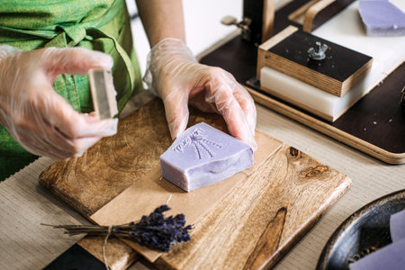 Close-up of hands pressing handmade lavender soap with floral stamp. Natural skincare, artisan soap making, organic beauty, sustainable living, eco-friendly conceptの写真素材