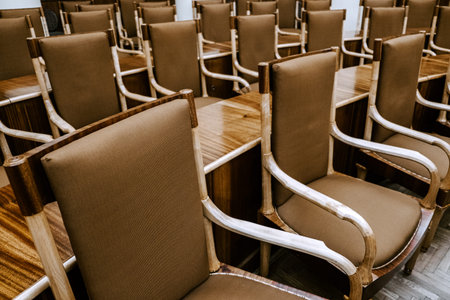 Rows of empty wooden chairs with fabric upholstery in a conference room, meeting or seminar setting,...