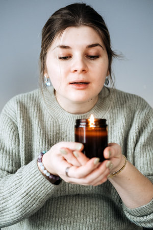 Woman holding a lit candle, embracing the warm and cozy essence of holiday hygge. Creating a calm...