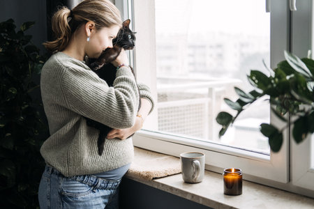 Woman embracing black cat by the window, representing mindfulness and pet therapy. Calm, soothing moment highlighting emotional well-being with animals.の写真素材