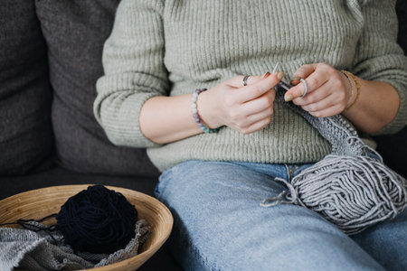 Pregnant woman knitting quietly on sofa, embracing self-care. Mindful crafting, relaxation, and slow living during pregnancy.の写真素材