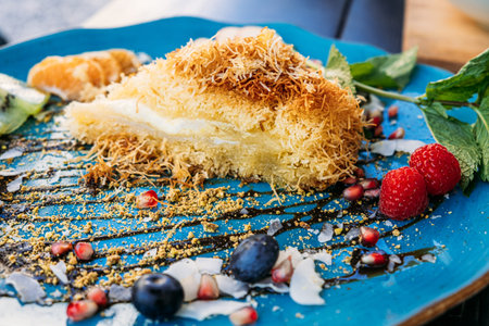 Elegant dessert with kunafa and fresh fruit slices on a blue plate. A creative presentation of...