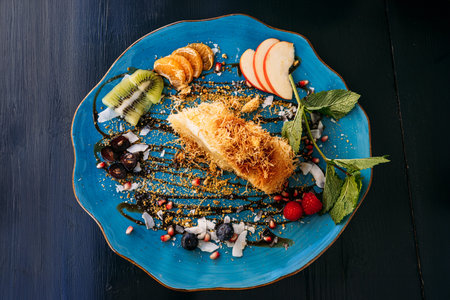 Elegant dessert with kunafa and fresh fruit slices on a blue plate. A creative presentation of...
