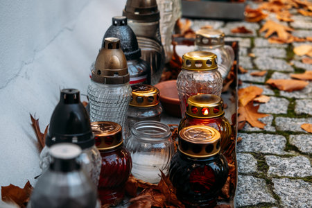 Row of remembrance candles with autumn leaves on a cobblestone path, evoking All Souls Day...