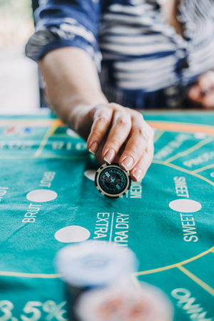 Hand placing a poker chip on a wine-themed casino game mat, blending gambling and wine culture for a...