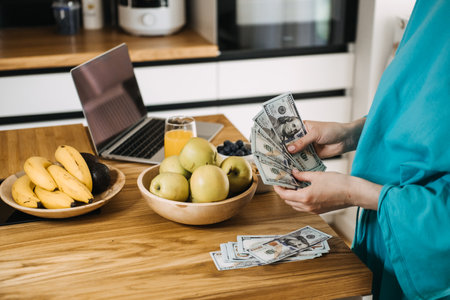 Woman budgeting money while preparing fresh meals in a cozy kitchen. Budgeting for healthy living, mindful spending, and cost-effective nutrition.の写真素材