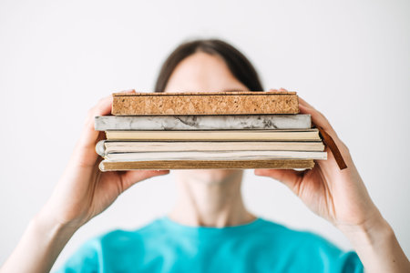 Young woman holding a stack of notebooks with unique textures and materials in a bright minimalist...
