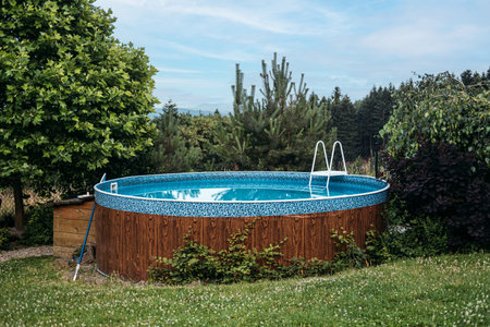 Above-ground backyard swimming pool surrounded by lush greenery, emphasizing outdoor leisure, summer...