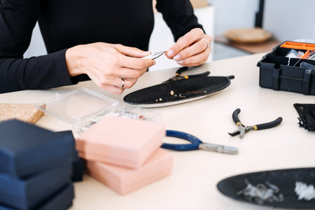 Close-up of a jewelry artisan assembling handmade earrings with precision tools. Independent jewelry...