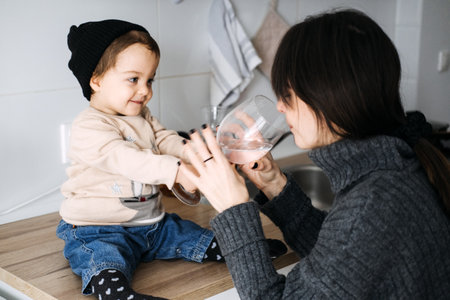 Mother and child sharing a drink in the kitchen, playful bonding moment. Family time, nurturing care, simple joys, domestic life, childhood connection.の写真素材