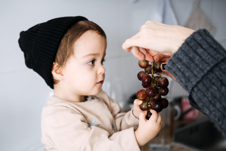 Mother offering toddler grapes, encouraging healthy eating habits. Toddler nutrition, early childhood development, family care, nurturing moments, healthy diet.の写真素材
