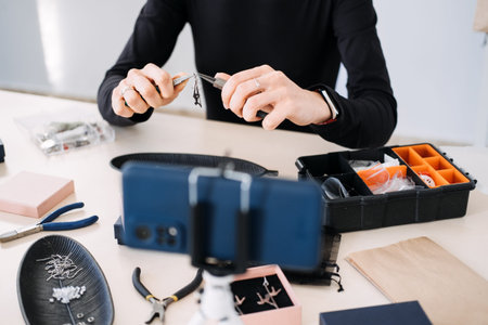 Handmade jewelry business owner recording a video tutorial with a smartphone. Content creation,...