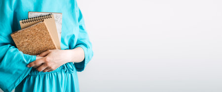 Close-up of woman holding a stack of natural-toned notebooks and her face behind a marble cover journal. Journaling as a wellness ritual, mindful living, emotional release, healing through writingの写真素材