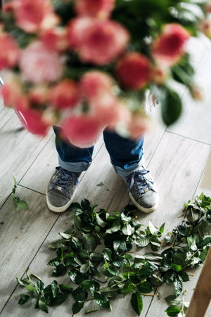 Florist standing over a floor scattered with green rose leaves after bouquet preparation. Revival of...