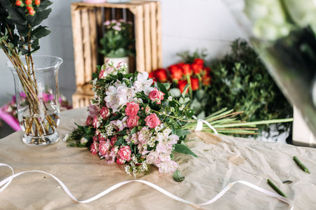 Hand-tied bouquet of pink flowers resting on a kraft paper work table in a flower shop. Social media marketing, florist branding, handmade bouquet, creative workspaceの写真素材