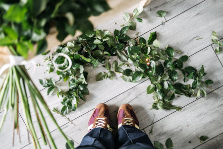 Overhead view of trimmed leaves scattered on studio floor beneath florists shoes. Flower arranging, artisan florist, bouquet making, creative processの写真素材