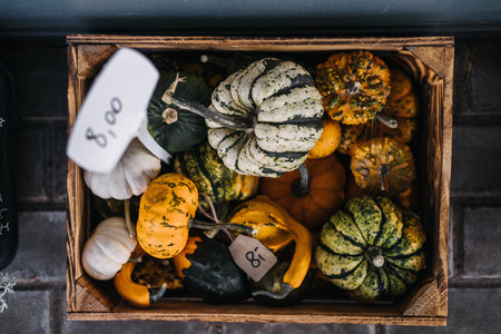 Top-down view of assorted ornamental gourds in a rustic wooden crate with handwritten price tags....