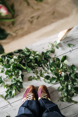 Overhead view of trimmed leaves scattered on studio floor beneath florists shoes. Flower arranging, artisan florist, bouquet making, creative process. High quality photoの写真素材