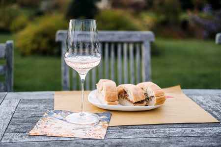 Glass of sparkling rose wine and rustic bread on a wooden garden table with a soft natural background. Food storytelling, rustic lifestyle, hospitality visuals, table styling inspoの写真素材