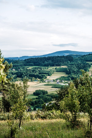 Scenic rural valley with cultivated fields, scattered houses, and tree-lined hills viewed from an elevated meadow. Countryside holidays, agritourism destinations, rural immersion, landscape serenity..の写真素材