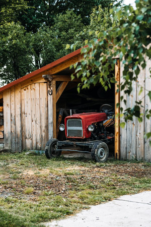A vintage tractor sits under a wooden shelter symbolizing enduring rural practices and small-scale agriculture..の写真素材