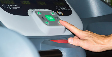 Male hand pressing button on treadmill in a gym.