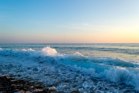 Sea waves breaking on a stony beach, forming sprays and splashes at sunsetの写真素材