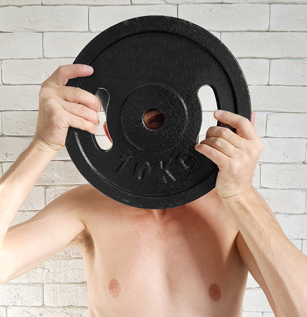 Close-up of young healthy man with big muscles holding disk weights in gym.の写真素材