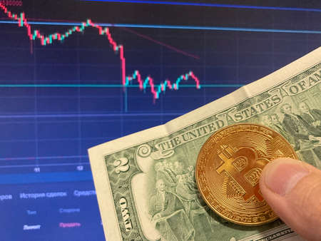Bitcoin coin on paper bill two Dollars, USD - blurred background. The electronic schedule of bitcoin, volume tradesの写真素材