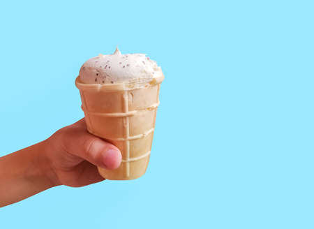 Fresh white ice cream in waffle cup in kids hand on blue backgroundの写真素材