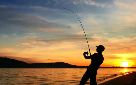 Young man fishing on a lake at sunsetの写真素材