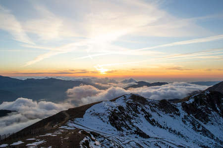 Snowy high mountains through the clouds in sunset skyの写真素材