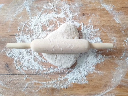 Wooden rolling pin and dough stretched on wooden table. top view.