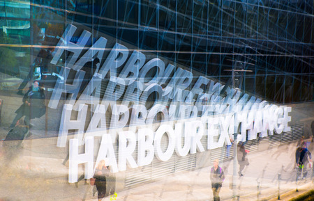 Multiple exposure effect image. Office workers walking against of Harbour Exchange signの写真素材