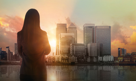 Young woman looking over the Canary Wharf business and banking aria with skyscrapers at sunset. Future, new business opportunity, freedom and stability. London, UKの写真素材