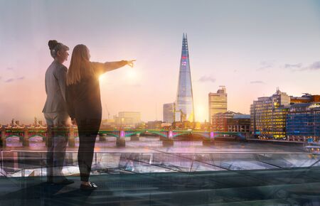 Two travellers with suitcases looking over the  City of London at sunset before departure. Future, new business opportunity, freedom and travelling concept. London, UKの写真素材
