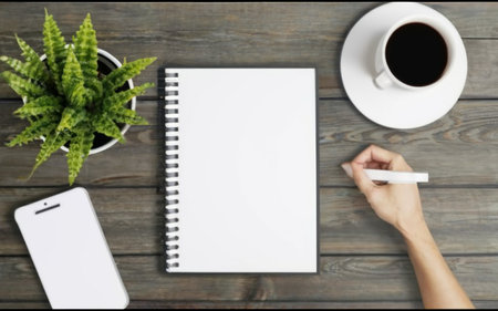 Top view of female hands writing on blank notebook with coffee cup on wooden tableの素材