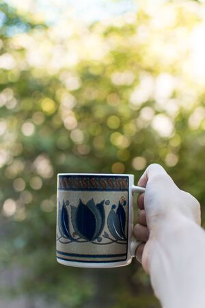 Hand holding a cup of coffe on a green nature backgroundの写真素材