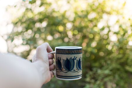Hand holding a cup of coffe on a green nature backgroundの写真素材