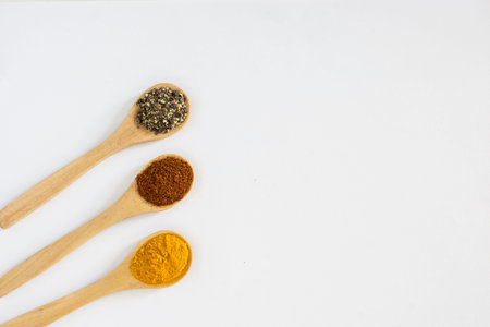 Turmeric, Paprika and Black Pepper ground in wooden spoon over white background.